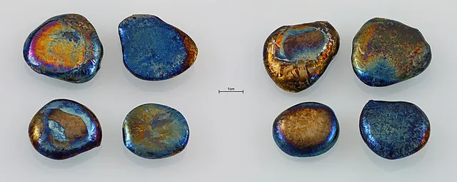 8 Pélets de hafnio con un poquito de óxido. El borde es azul electrico y el centro tiene tintes rojizos y amarillos