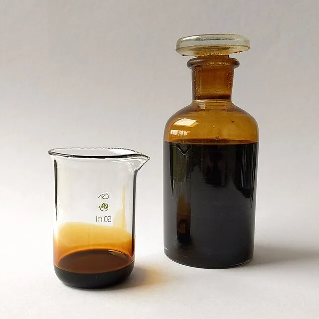 Una botella de petróleo y un pequeño matraz con el mismo contenido sobre un fondo blanco.